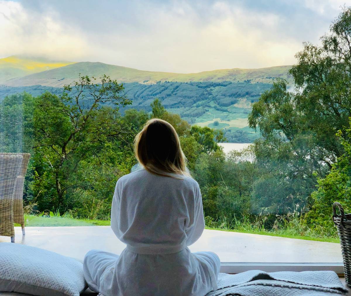 Woman sitting peacefully in a sunlit forest during a Quiet Retreat, eyes closed, hands resting on knees